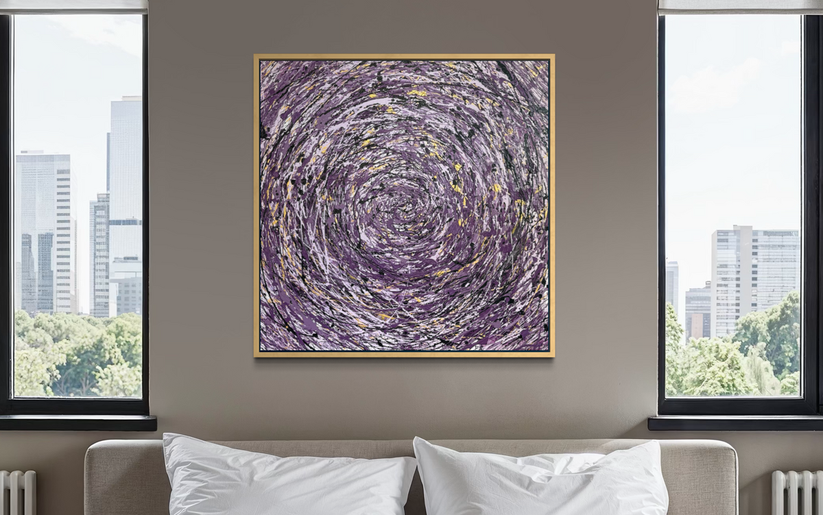 A square framed abstract art print featuring a swirling purple and gray vortex pattern with gold flecks, displayed on a neutral gray wall above a bed with white pillows between two windows showing a city skyline.